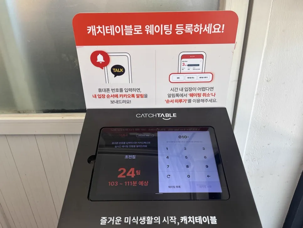 キャッチテーブルの店頭の順番待ちの機械。画面の右側に「010-」と番号を入れる数字キー、左上に言語を切り替える「LANGUAGE」のボタンがある。上の案内板には、携帯番号を入れると順番をカカオトークで知らせること、時間内に入れないときは順番待ちの取り消しや順番を後ろにずらす機能を使うよう書かれている