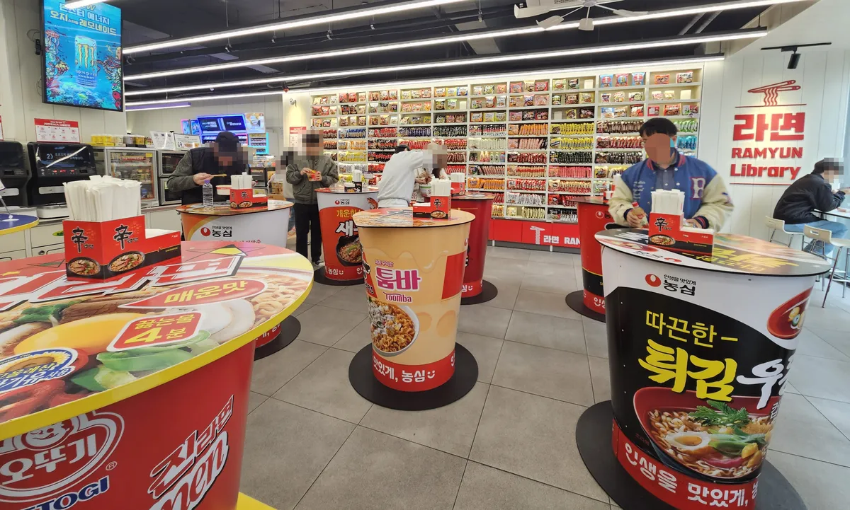 CUのラーメンライブラリーの店内。壁一面のラーメンと、カップ麺の形のテーブル