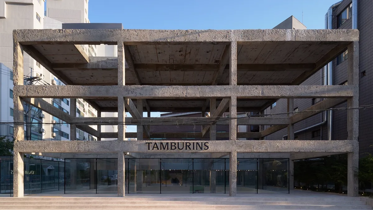 TAMBURINS聖水店の外観。コンクリートの骨組みに看板、1階はガラス張り