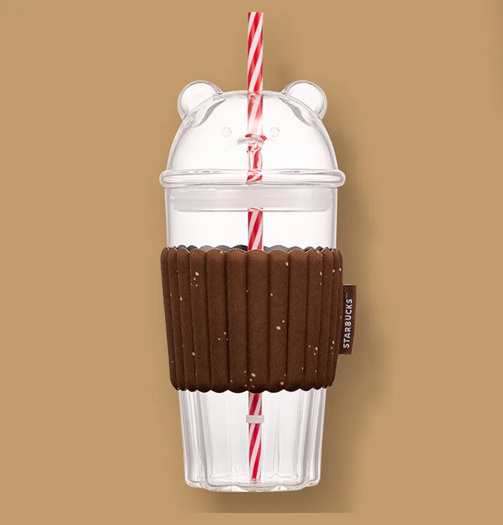 クマの形のふたと赤白のストローがついた、茶色いスリーブのガラスのカップ