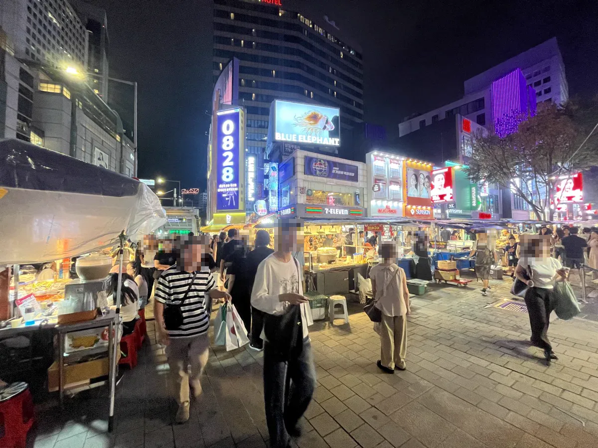 明洞の商店街に明かりがともり、食べ物の屋台が並ぶ夜の風景