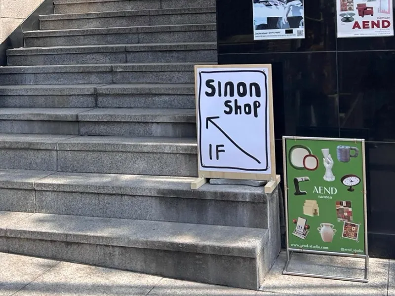 階段の下に置かれた「Sinon Shop 1F」の手書き看板