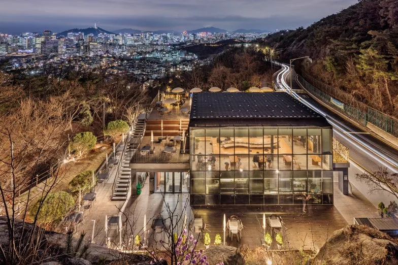 夜の草所冊房。ガラス張りの建物の向こうに南山タワーとソウルの街