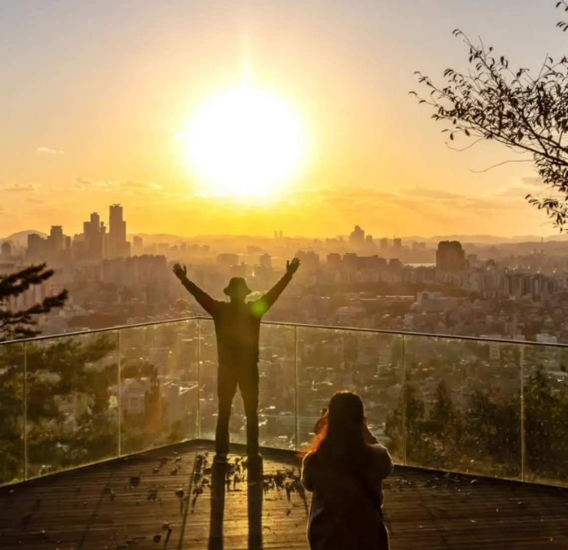 ガラスの柵の前で両手を広げる人のシルエットと夕日