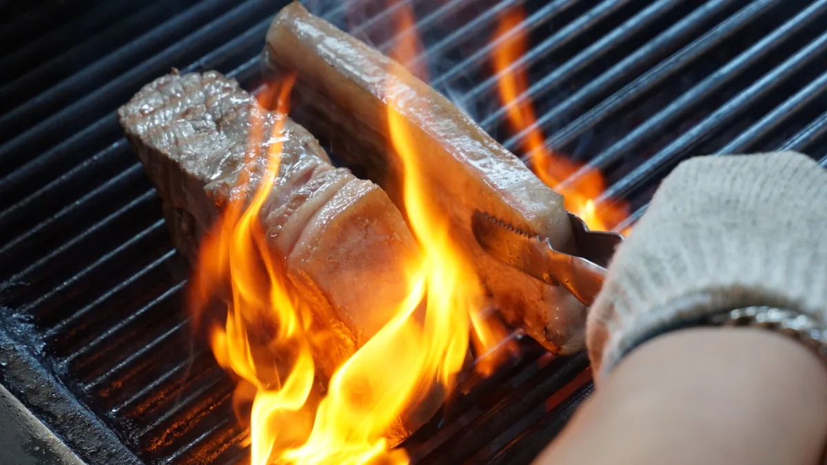 練炭の炎で下焼きされる厚切りの豚肉