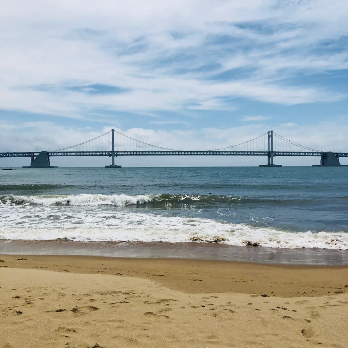 広安里海水浴場 — 波越しに望む広安大橋