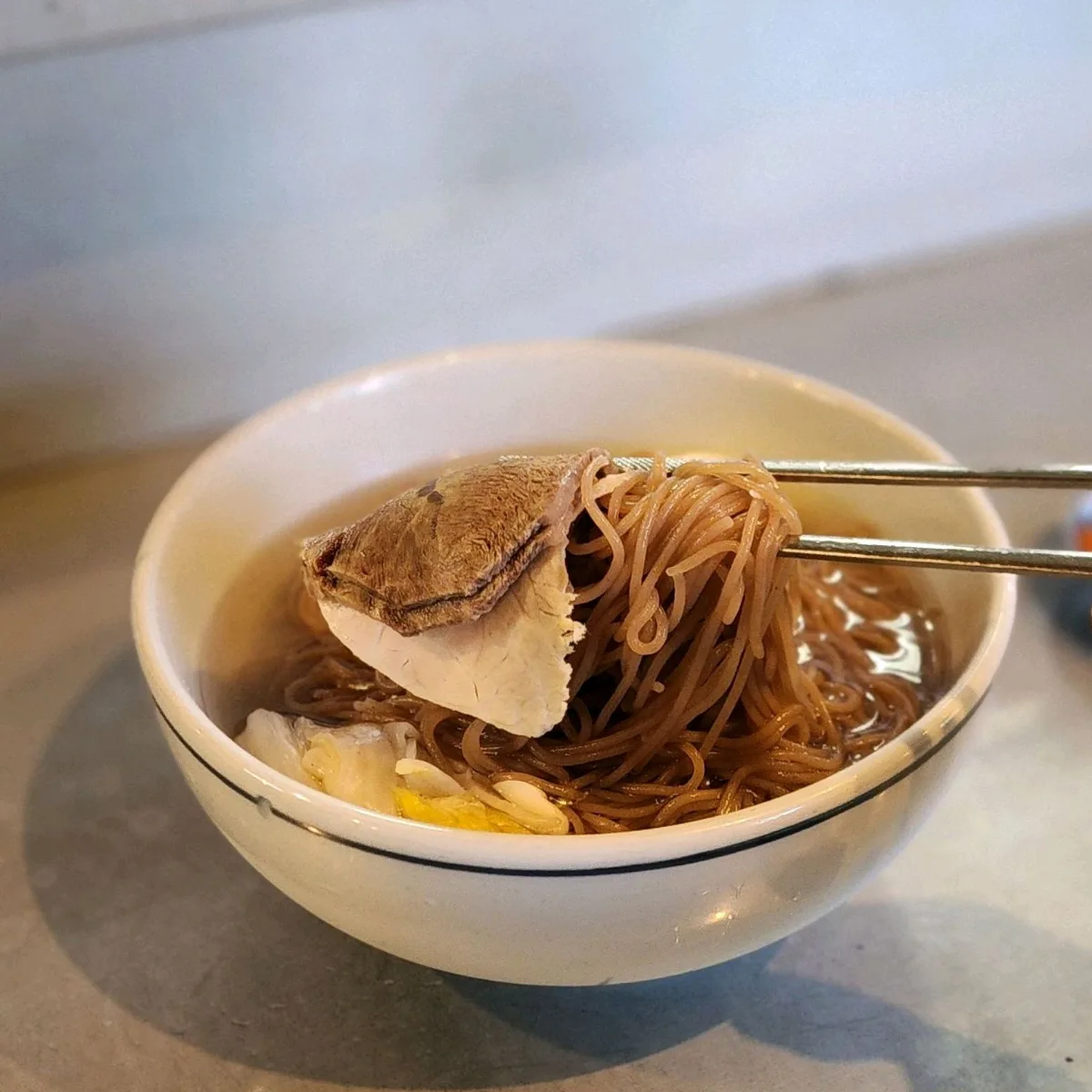 光化門クッパ 本店 — 箸で持ち上げた冷麺と肉