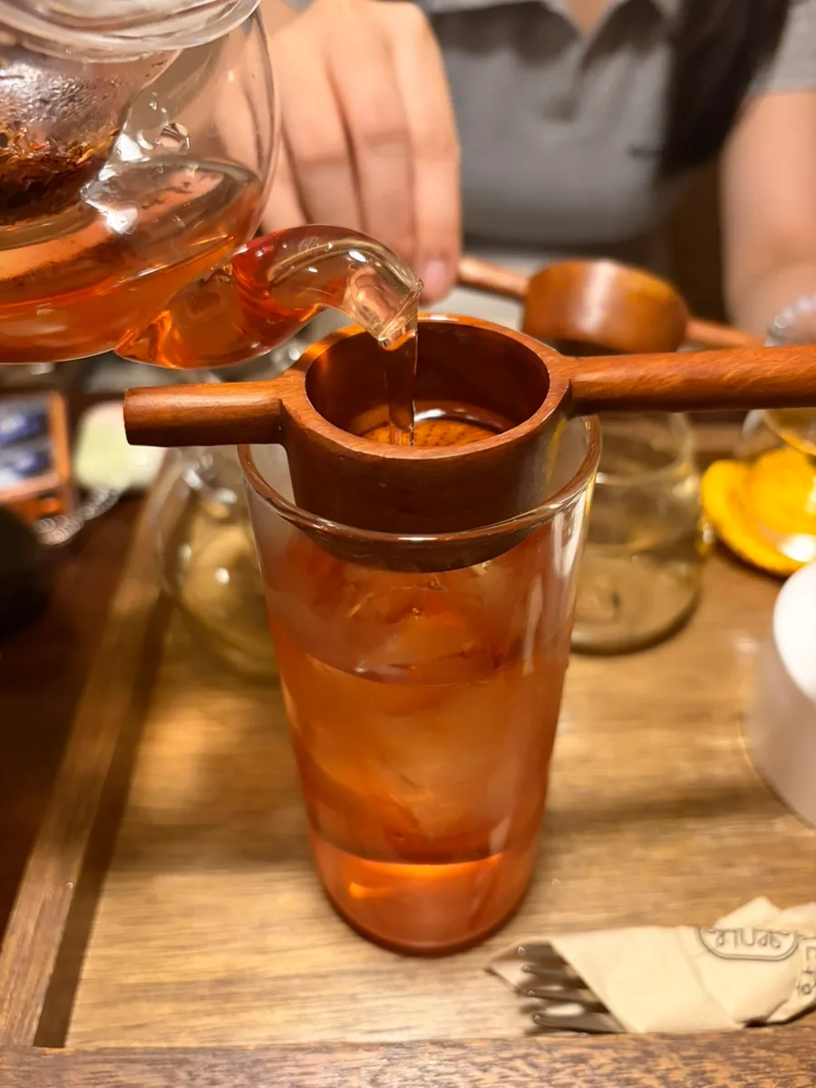 木の茶こしで氷のグラスに注ぐお茶