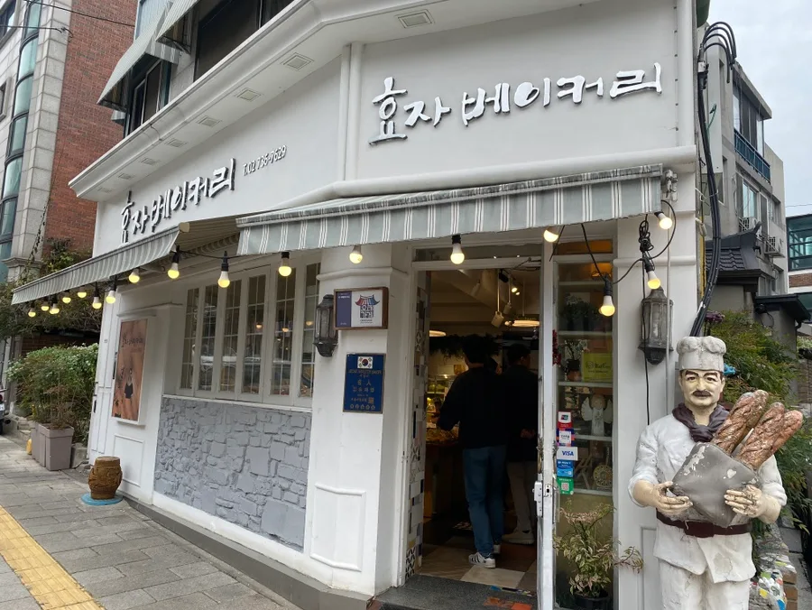 孝子ベーカリー — 白い壁とパン職人像の店舗