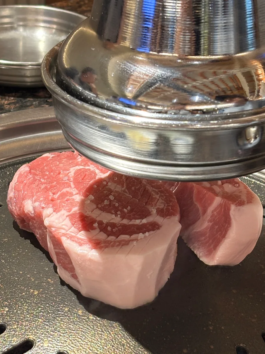 塩をふった厚切り肉を鉄板で押さえる