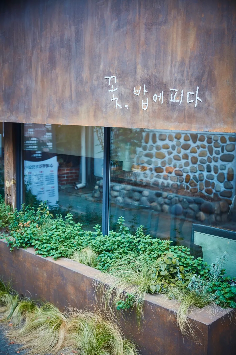 植え込みの奥にある店名の壁