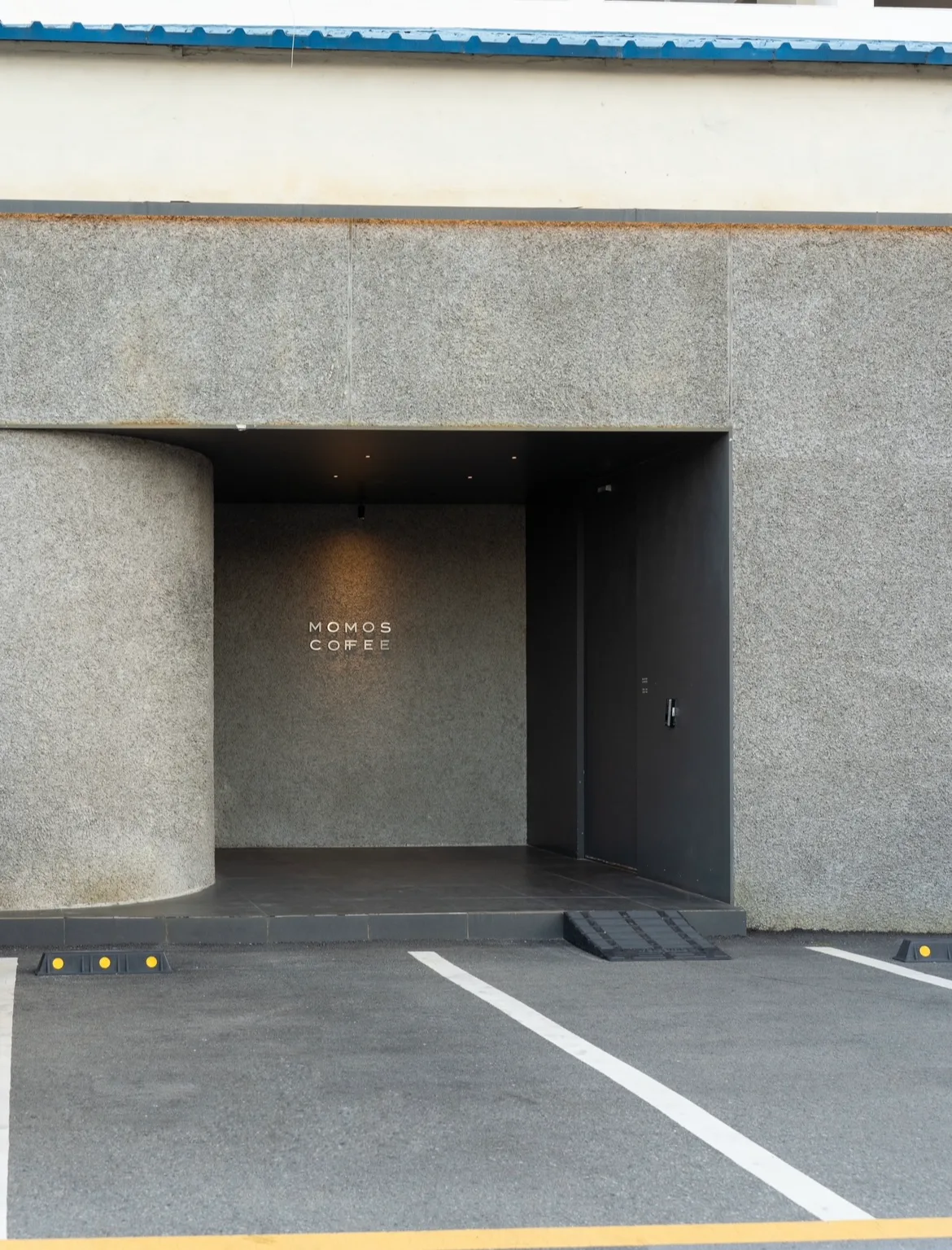 MOMOS COFFEE 影島店 — モモスロゴのある石壁入口