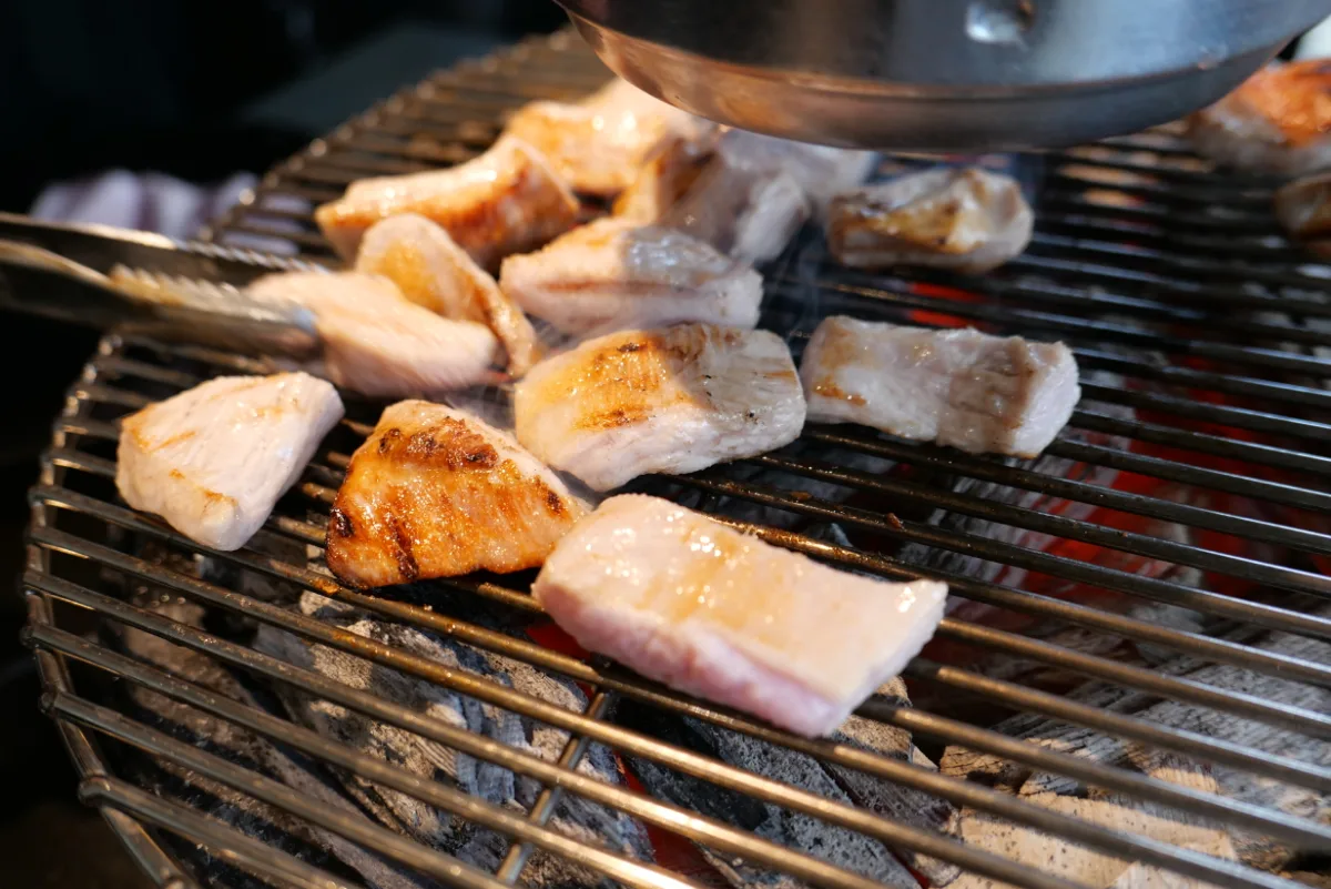 炭火の網で焼ける豚肉