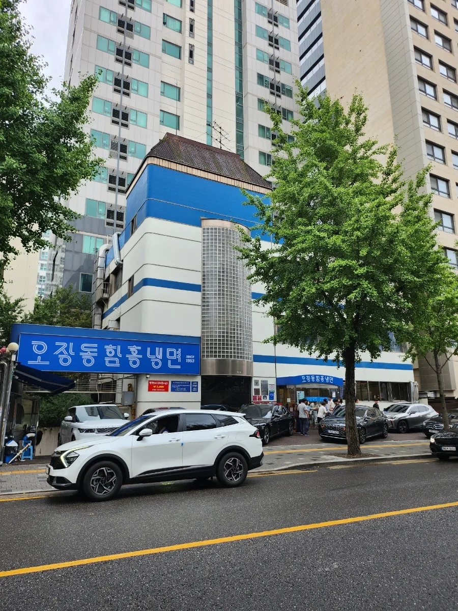 五壮洞咸興冷麺 — 街路樹越しの青白い店舗