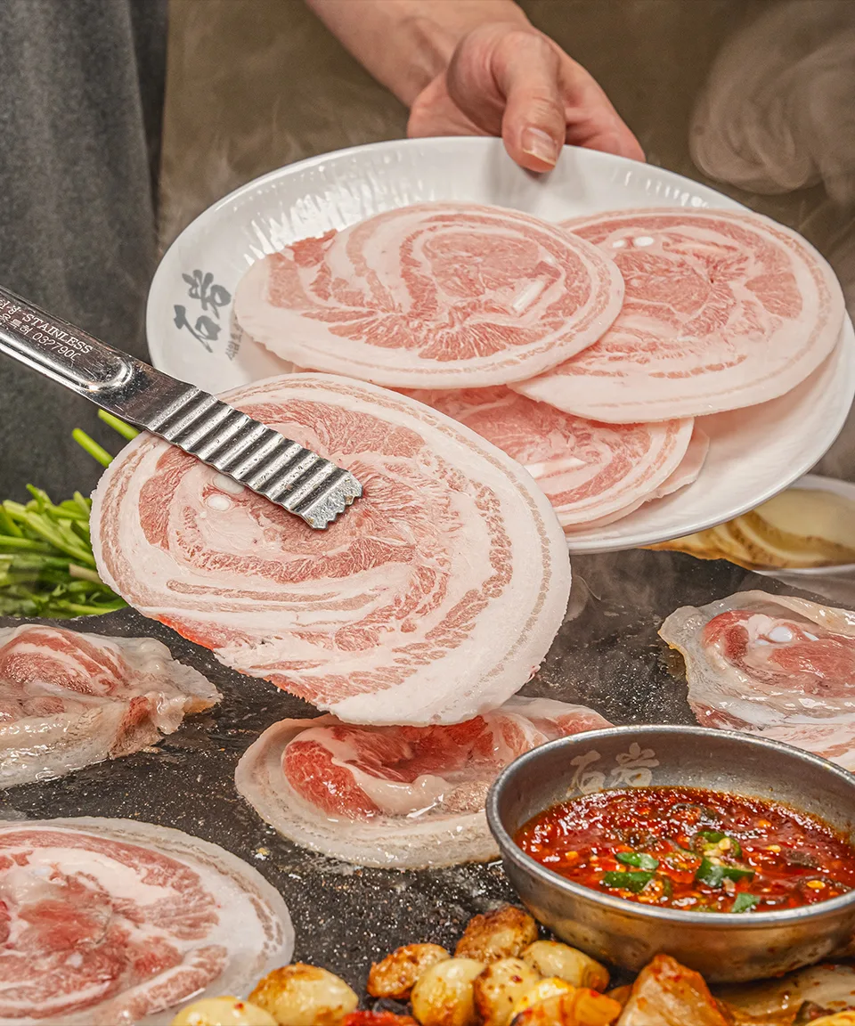 厚切り豚肉をトングで運ぶ手元