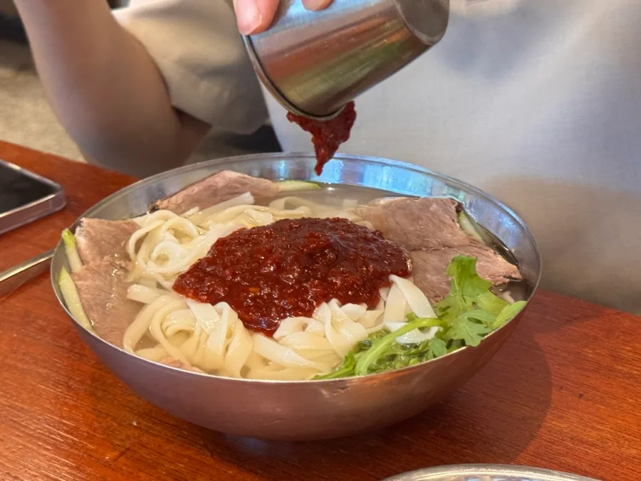冷たい麺に辛味だれを注ぐ手元