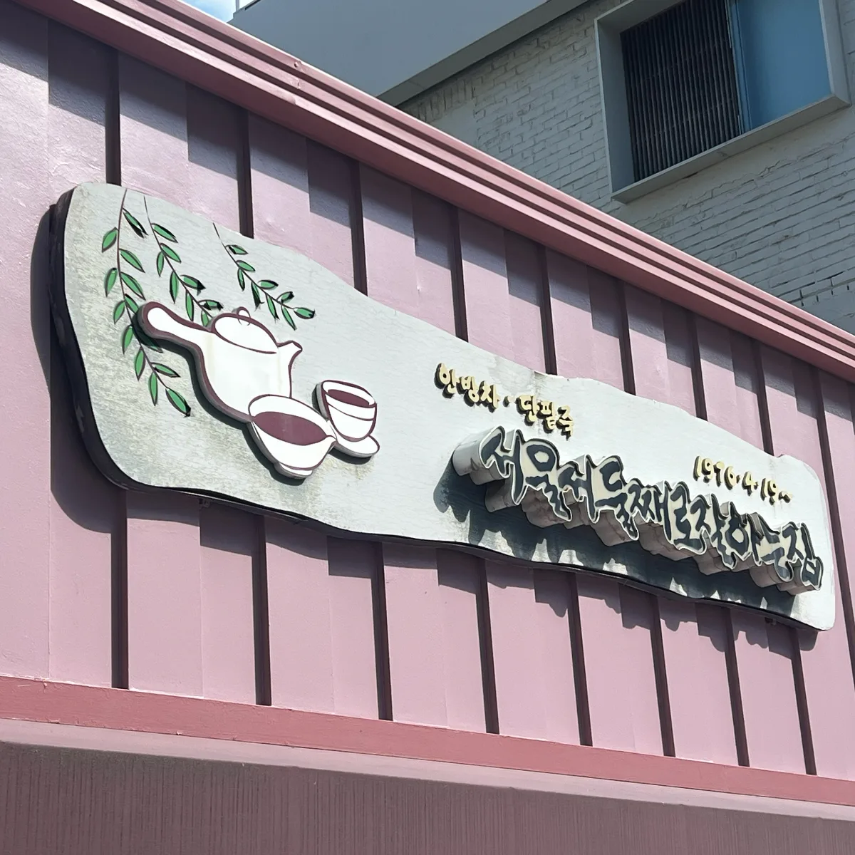 桃色の壁に掲げた店名看板