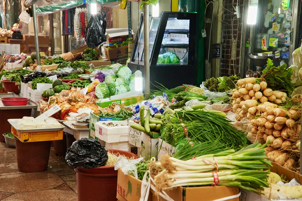 新浦国際市場 — 葉物野菜と根菜が並ぶ青果店