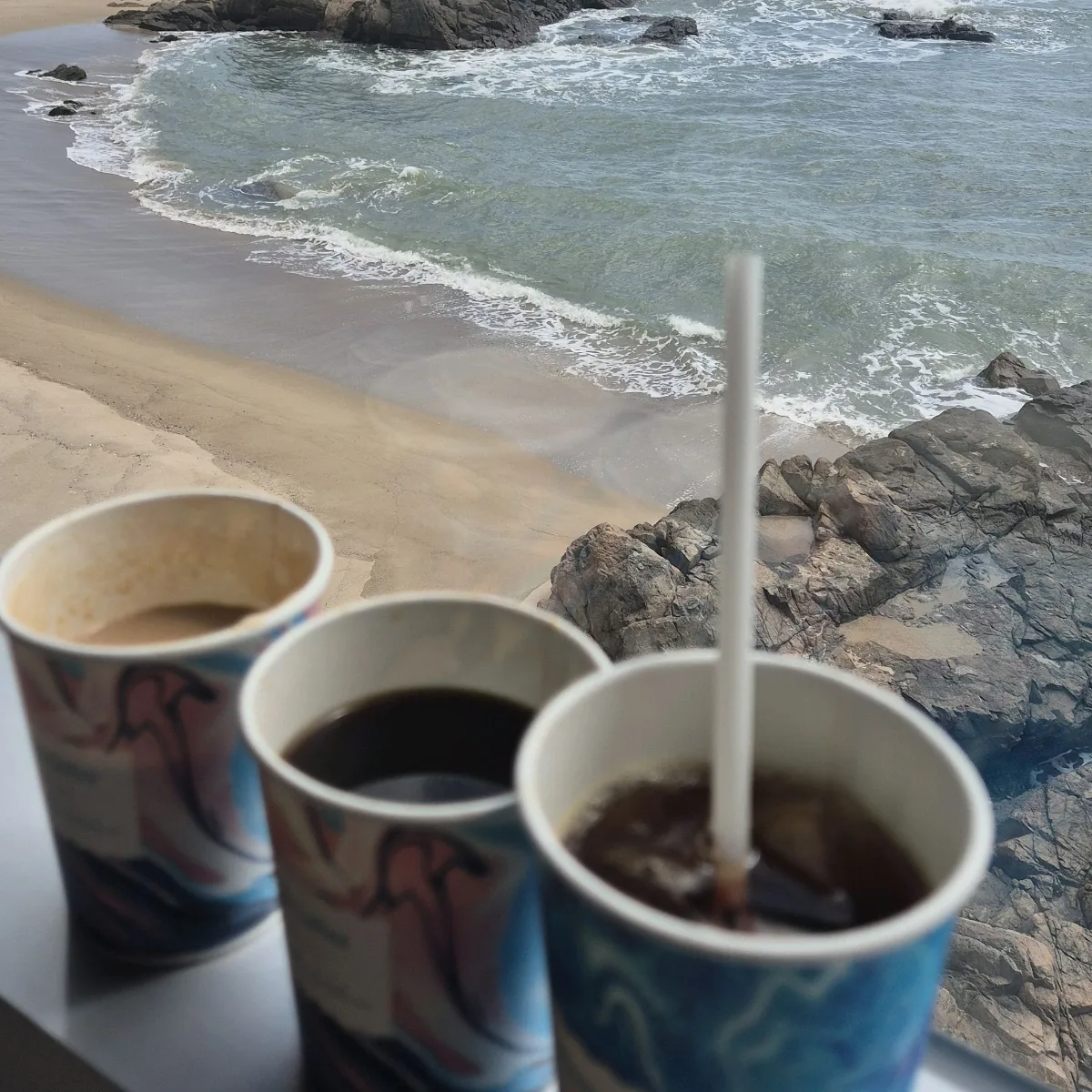 岩場の海を望むテーブルのコーヒー3杯
